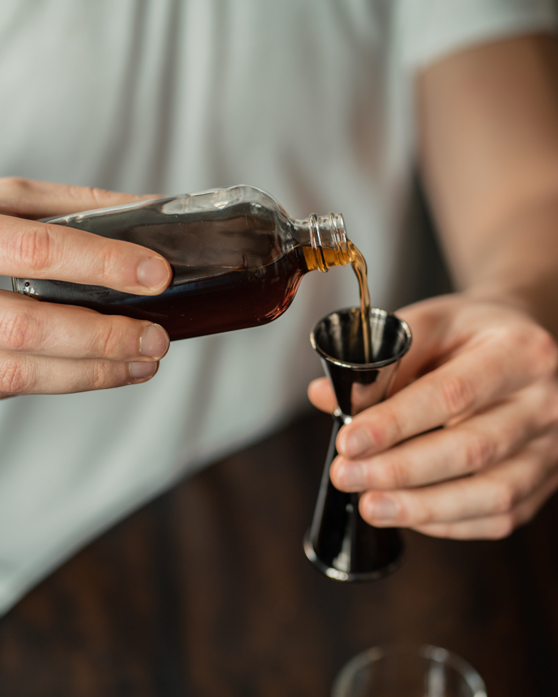 Pouring Dmerara Syrup into a jogger for a cocktail